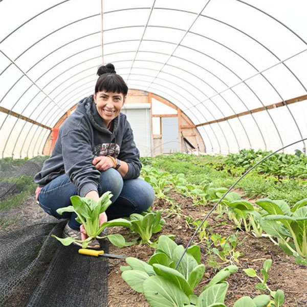 women in green house kneeling next to baby plants